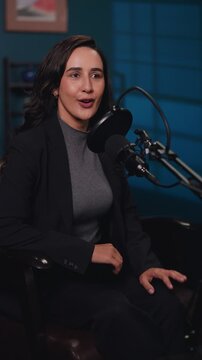 Portrait of brunette woman conducts podcast show in recording studio vertical shot. Lady host talks in mic during interview in radio office. Telecommunication