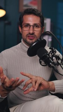 Portrait of young man talks and gestures during podcast show in audio studio vertical shot. Professional host conducts broadcast in multimedia company office