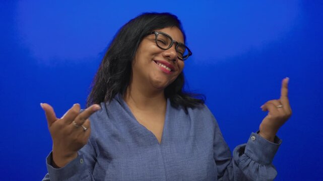 African american woman smiles and shows middle finger in blue studio; insult defiance rebellion boldness.