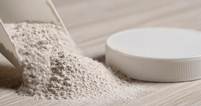Close-up of spilled white powder from a scoop beside a round container on a wooden surface
