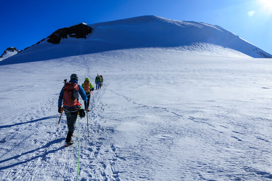 Mountaineers in rope team with crampons ascending towards mountain summit Parrotspitze and glacier panorama in the morning in Pennine Alps, Italy