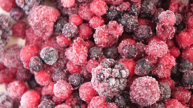 Close up frozen berries mix with raspberries, blueberries, and blackberries covered in ice crystals slowly rotating in dynamic motion