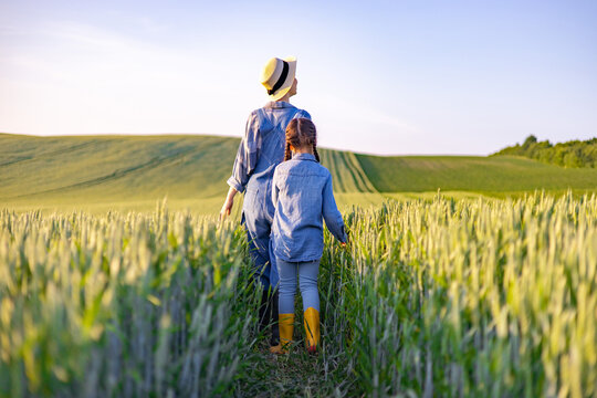 A mother and her daughter walk through a golden wheat field under a clear blue sky, enjoying a serene rural landscape