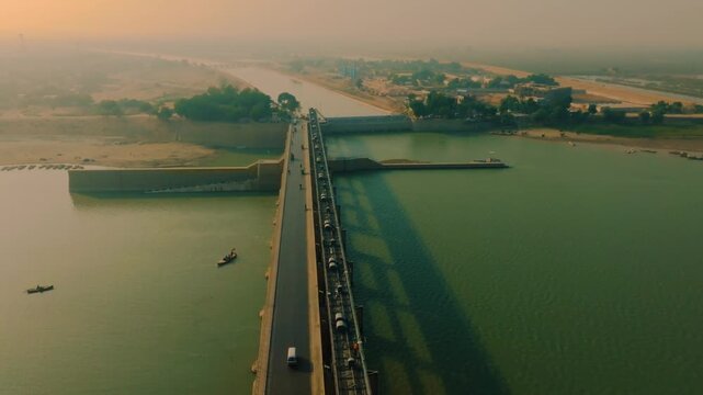 Kotri Barrage in Sindh, Pakistan during a hazy afternoon sunset. Traffic on the bridge and intense green river water below. Fast forward aerial glide in 4K.