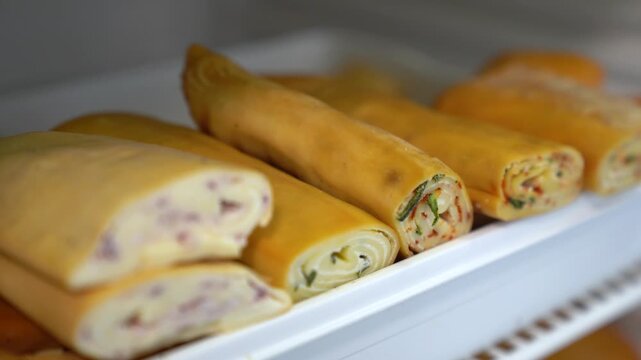 Delicious homemade cheese rolls with various fillings, ready for serving or packaging, Savory cheese roulade in a tray, offering fresh snacks or appetizers for sale
