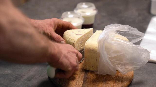 Hands slicing artisan cheese block on wooden board preparing dairy products