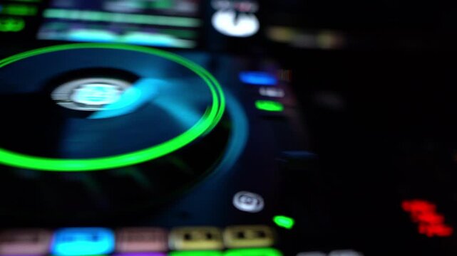 DJ controller with illuminated jog wheel during live club performance. Electronic music mixing setup with glowing interface and nightclub atmosphere.