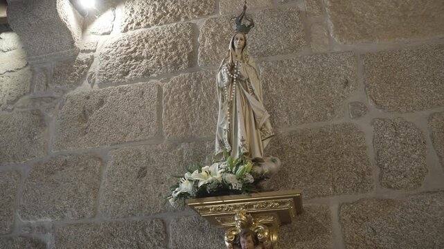 Statue of Virgin Mary with rosary on golden bracket against rough stone church wall