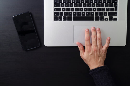 Top View of Hand Using Laptop Trackpad with Smartphone on Desk