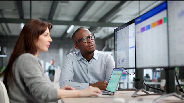 Two Young Professionals Use ERP And CRM Software On Multiple Computer Screens