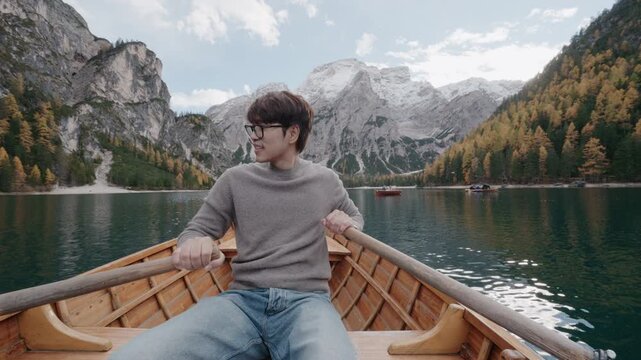 A man sitting in a traditional wooden boat on the turquoise waters of Lago di Braies in the Dolomites, Italy. Scenic alpine lake surrounded by mountains during summer vacation.