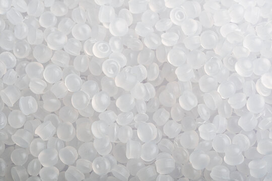Translucent plastic pellets fill frame in soft light, clean industrial background for polymer production and recycling themes.