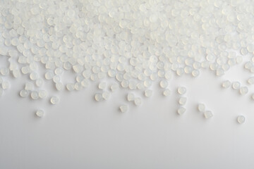 Translucent polymer pellets scatter across white surface, industrial background with copy space for...
