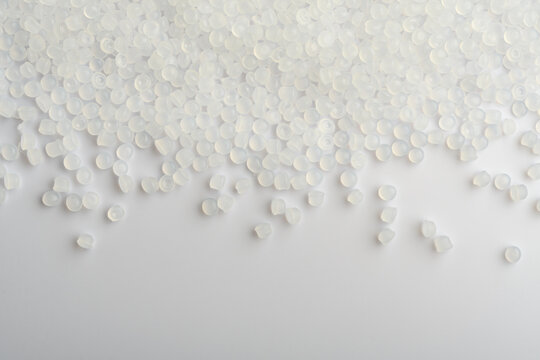 Translucent polymer pellets scatter across white surface, industrial background with copy space for plastic production concept.