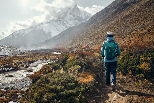 A brave female trekker with a backpack walks on mountain and river, path towards Dingboche village, surrounded by snow-capped Himalayan peaks during Everest Base Camp trek, Nepal.