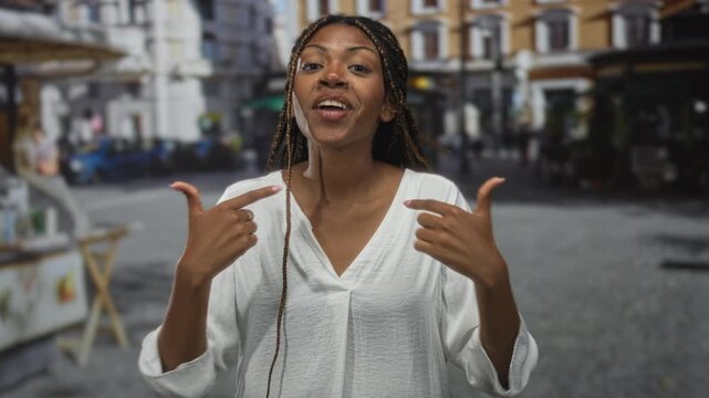 Woman points finger to chest on urban cobblestone street wearing white blouse and braids; confidence self affirmation.