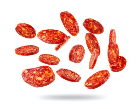 Slices of red-orange pepperoni sausage are suspended mid-air with shadows underneath, set against a white background
