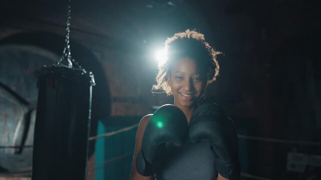 Joyful athletic woman smiling to camera in boxing ring, young female box fighter . Medium portrait of african american sportswoman in fight club, do combat sport for good body shape and self-defense