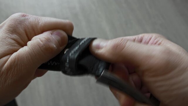 Person hands meticulously manipulate black leather strap using specialized metal tool. Close up highlights intricate stitching, craftsmanship, and repair or creation process.