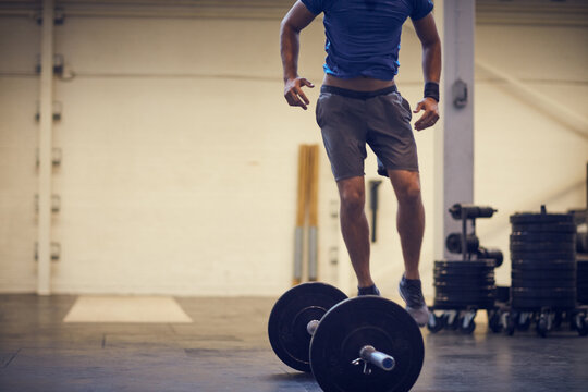 Legs, athlete and jump over barbell at gym for burpees exercise, intense cardio and endurance. Feet, man and body movement with weights at health club for functional fitness, agility and coordination