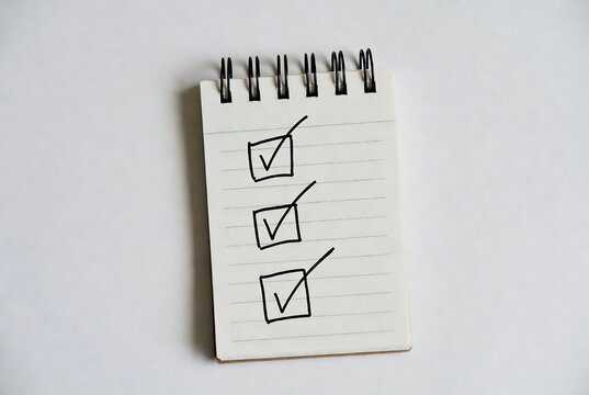 A notepad with three checkmarks. Someone is checking off items. A white surface serves as the background.