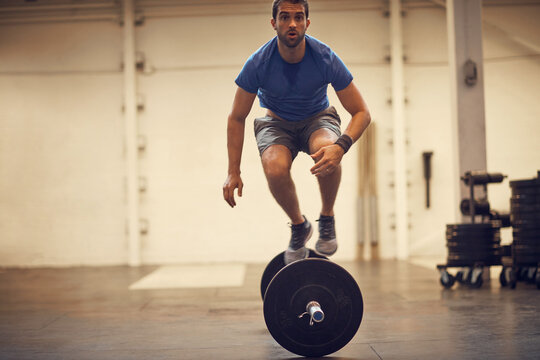 Fitness, athlete and jump over barbell at gym for burpees exercise, intense cardio or endurance. Energy, man or plyometric with weights at health club for functional training, agility or coordination