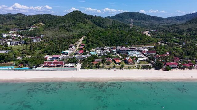 Cinematic aerial view of Klong Nin Beach in Koh Lanta, Thailand. The drone video captures blue waters, sandy shores, and lush greenery under a sunny sky.