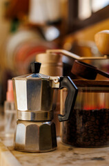 Ingredients for making coffee. Moka pot, bean spray, coffee grinder with coffee beans standing on the kitchen table.