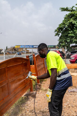 Fototapeta premium African male carpenter using a spray gun to varnish wooden bed frame in his workshop, furniture finishing