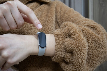 A woman's finger touching the screen of a grey smartwatch, wearing a brown fuzzy teddy jacket. © Iuliana