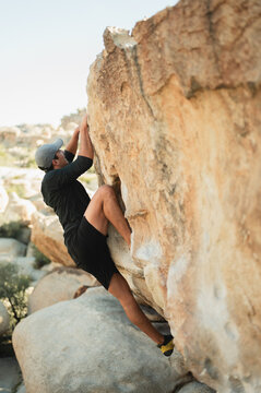 Young happy climber pulling toward top of boulder in Joshua Tree