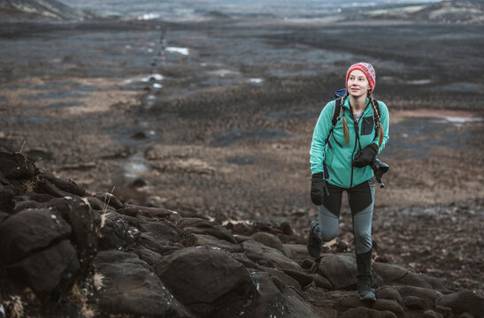 Young woman with camera hikes in lava field, Helgafell, Iceland