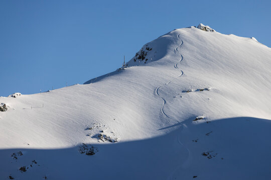 A single ski track carves way down mountain side in sunshine