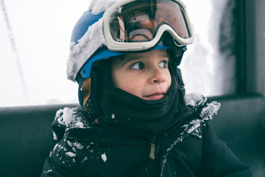 Young boy snowboarder smiles and looks out gondola window
