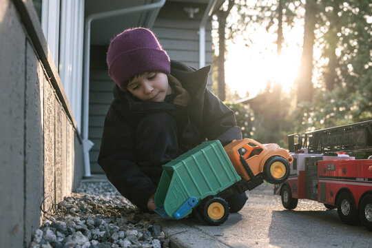 Young boy plays with toy truck outside house on sunny fall day