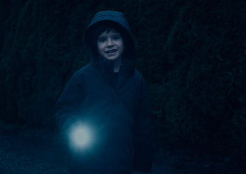 Young boy shines flashlight at camera and smiles on evening fall day