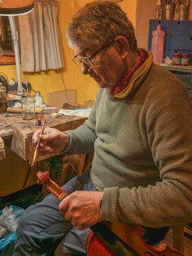 Luthier carefully varnishing violin scroll at workshop