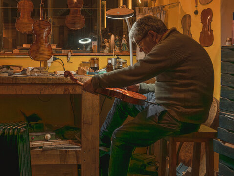 Luthier carefully varnishing scroll of violin in workshop