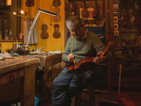 Luthier creating art varnishing scroll and body of a handmade violin