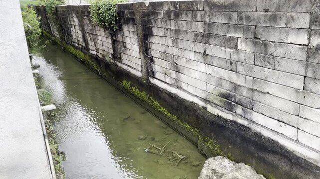 Old weathered concrete wall by a drainage canal in a residential area