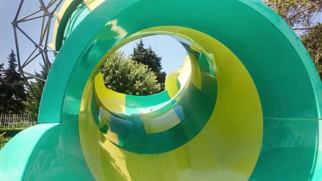 Happy girl riding down on colorful water slide at Aquapark. Little girl at water park. Summer vacation fun, adventure, and recreation at an aquapark.