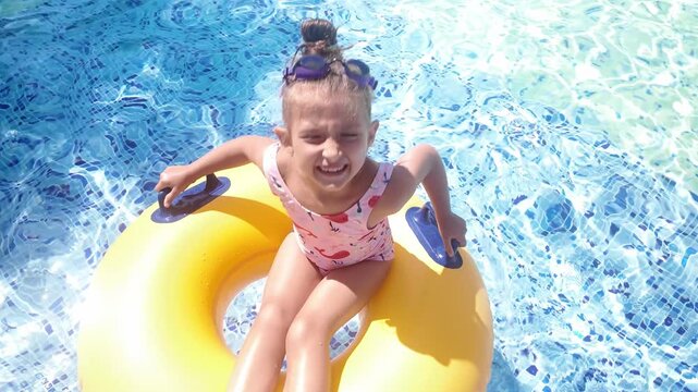 Happy little girl relaxing on inflatable ring in swimming pool, joyful summer vacation, child enjoying water fun and leisure activity under bright sunlight