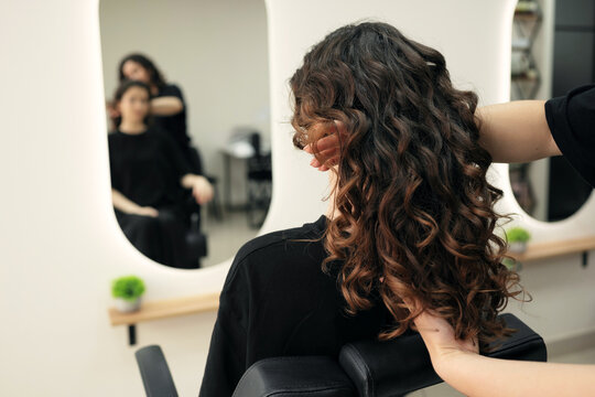 Professional stylist showing perfect curly hair result in a specialized salon mirror. Healthy textured ringlets styled with curly girl method for maximum volume and shine.