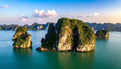 Poster Reflectie Scenic seascape featuring limestone karsts covered in lush greenery, reflected in calm turquoise waters under a partly cloudy sky  © Dolan