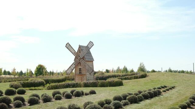 Wooden windmill in manicured garden with round boxwood bushes and green grass