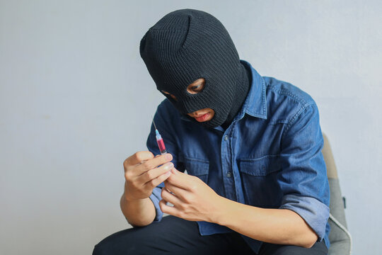 Masked Man Holding Syringe with Red Liquid, Symbolizing Drug Addiction and Crime