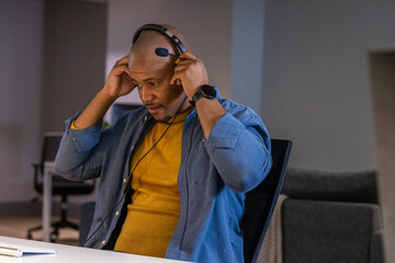 African American man adjusting headset in office wearing mustard tee, blue shirt, watch, keyboard © wavebreak3