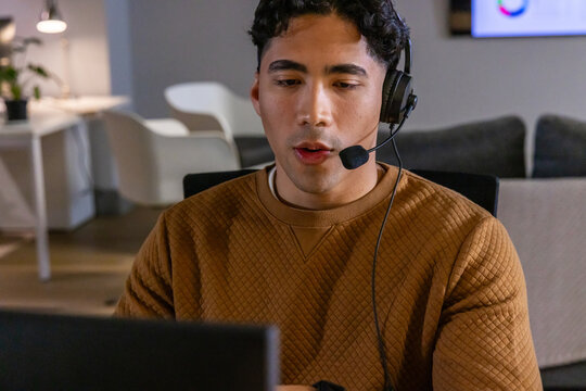 Male support rep wearing brown quilted sweater speaking into headset while viewing laptop at desk
