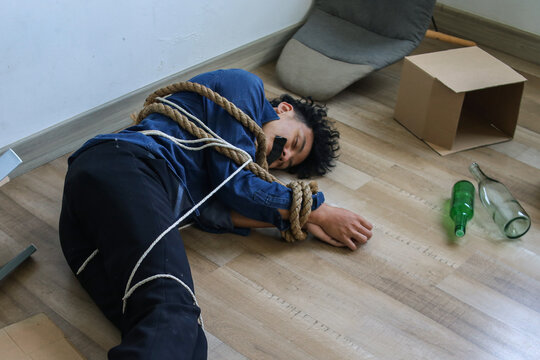 Male Hostage is Lying on Rope in Empty, Cluttered Room Filled with Boxes