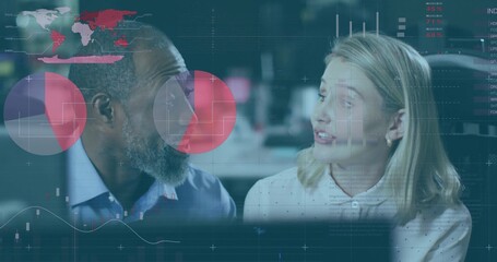 Discussing colleagues reviewing charts at office desk, in collared shirt and blouse, monitors shown
